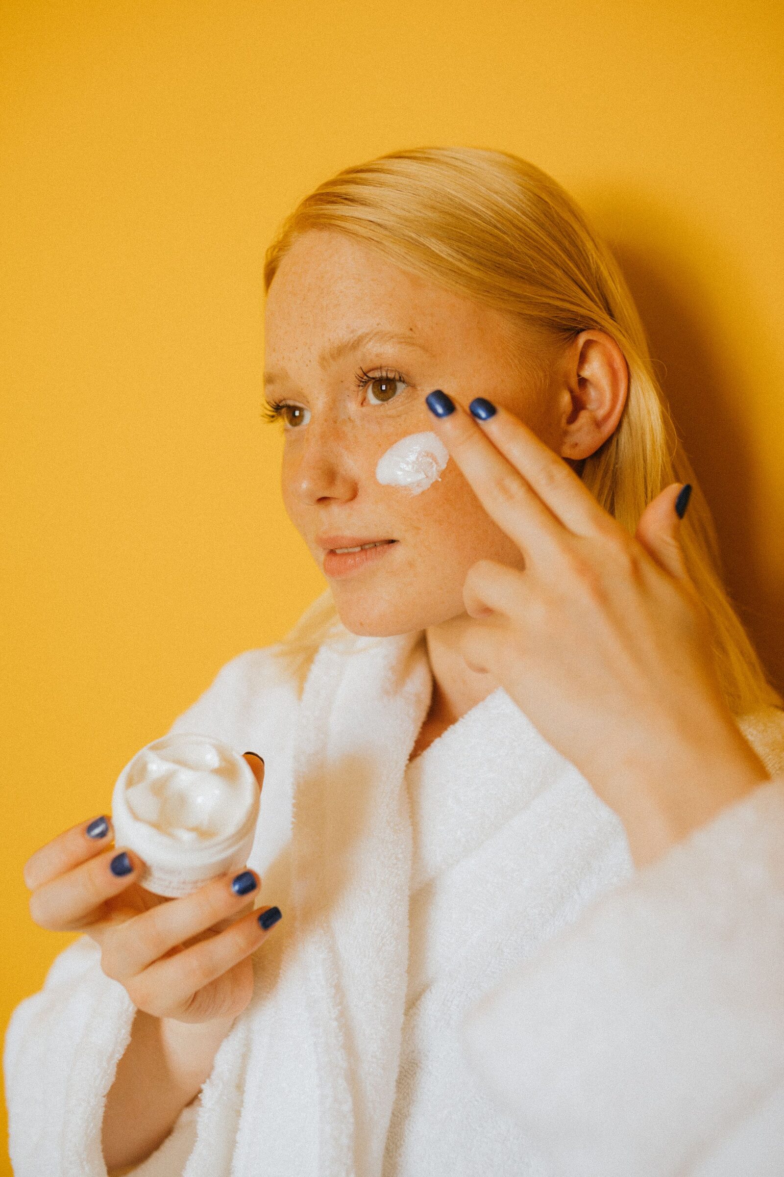 Model applying face cream against a yellow background