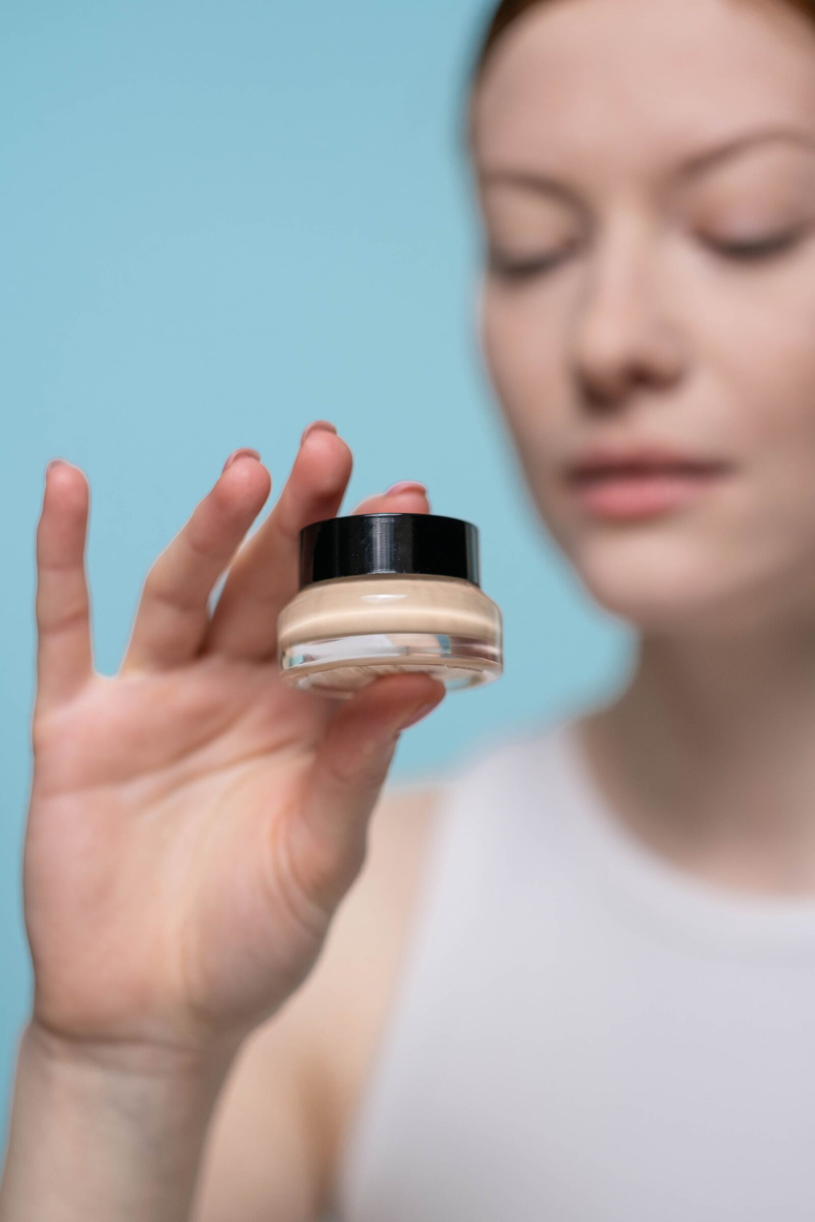 Cream jar held toward the camera against a blue background